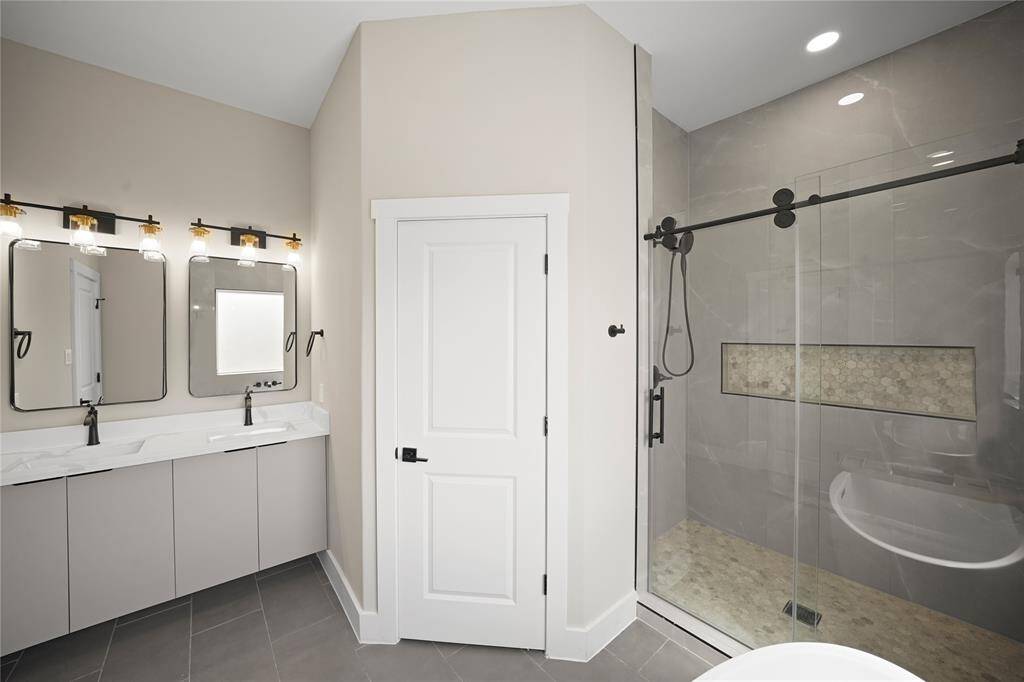 Check out the primary bathroom! Highlighted by an amazing glass enclosed shower with gorgeous tile, recessed lighting, double sinks, quartz countertops, and framed mirrors.