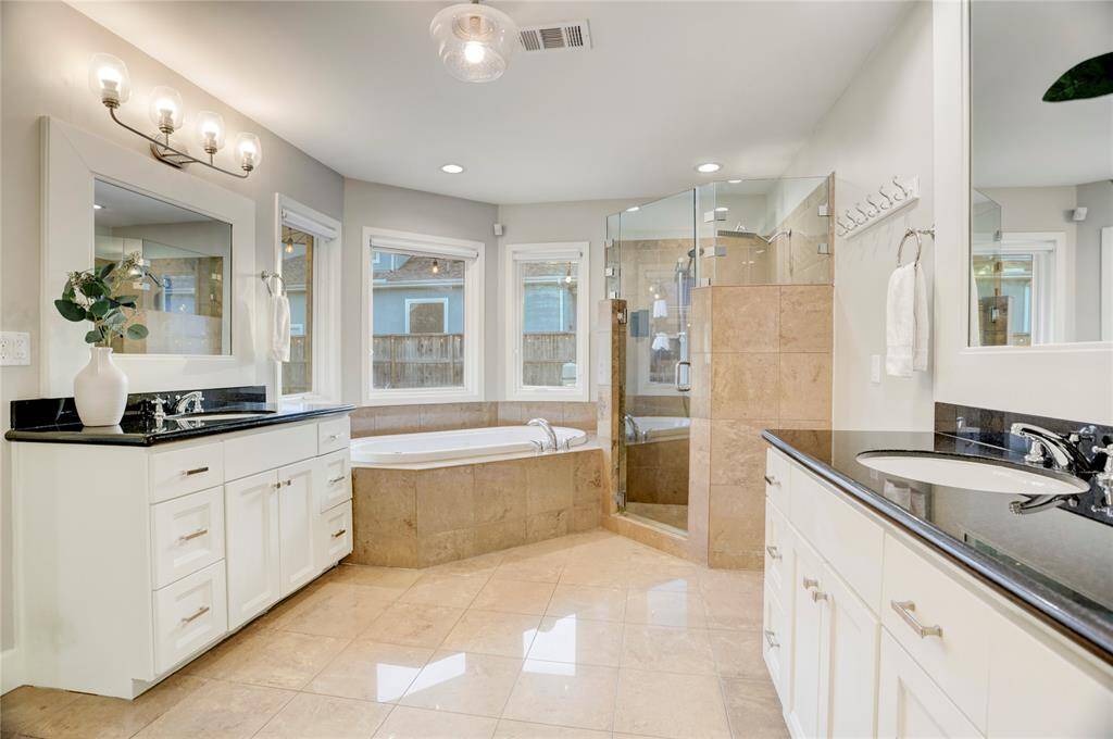 The spacious Primary Bathroom features 2 separate vanities with custom cabinetry & polished nickel hardware, timeless black granite countertops, large mirrors with custom wood trim, a soaking tub, a large, walk-in shower with oversized shower head & shower wand, large windows with custom window coverings, an enclosed toilet room and LED recessed lights.