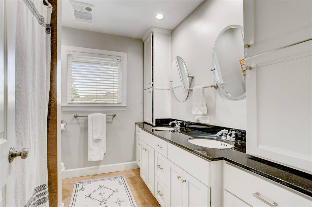 The Secondary Bathroom features timeless black granite countertops, 2 chic mirrors, custom cabinetry, polished nickel hardware, a tub/shower with 2 shower heads and LED lights.