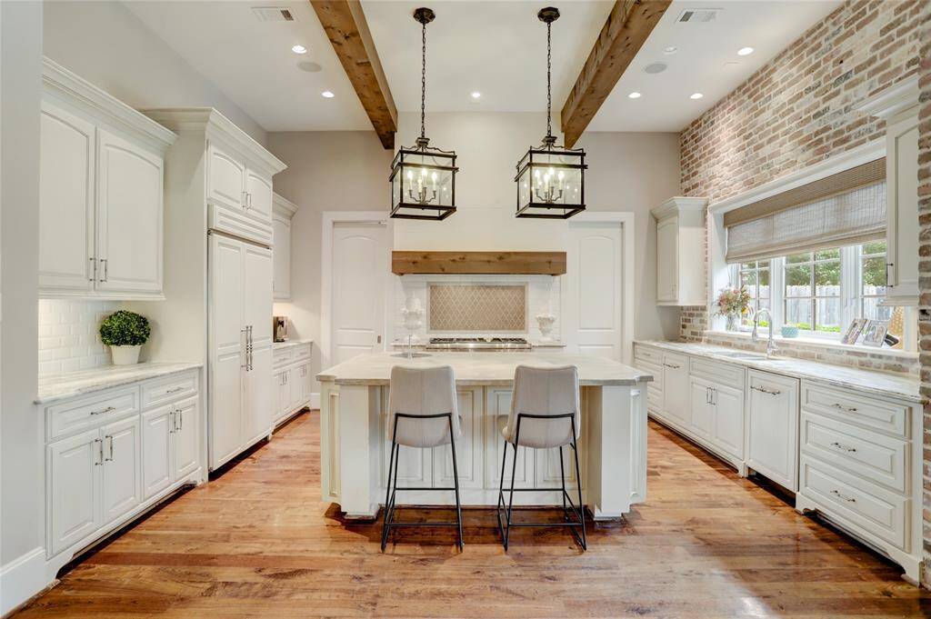 Large gathering island in this Chef's kitchen with continued wood beams and brick accented wall noting door to mudroom on the left and door to the pantry on the right