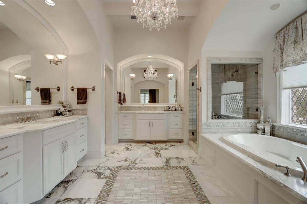 Primary bathroom retreat with marble counters and flooring and separate vanity areas.