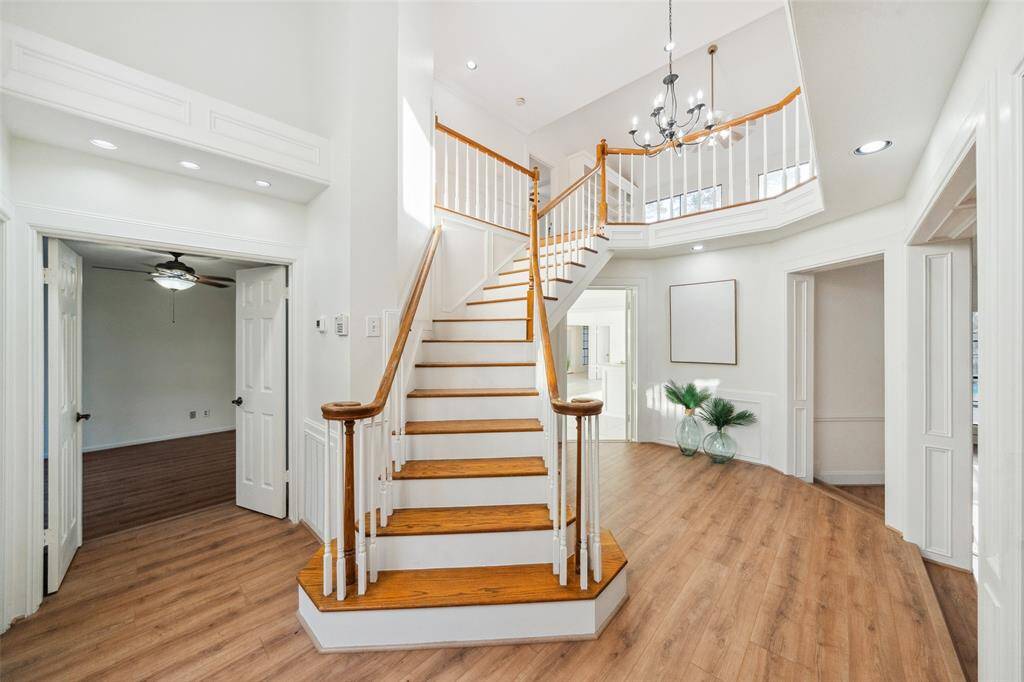 Elegant entrance featuring a grand staircase with wood flooring and railing, double-height ceiling, and sophisticated woodwork.