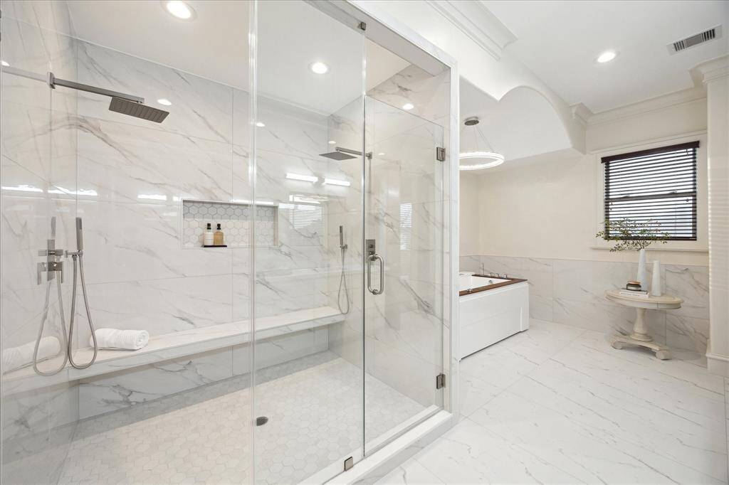 The functionality of dual shower heads and built-in seating complement the sleek aesthetic of marble and glass finishes.