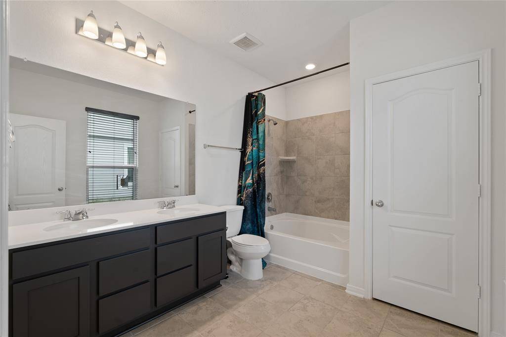 Elegant primary bathroom featuring a double vanity, sleek fixtures, and a spacious bathtub with a modern tile surround.
