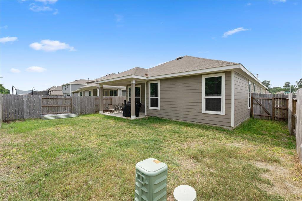 This photo shows a modest backyard featuring a covered patio attached to a single-story home with beige siding. The yard is enclosed by a wooden fence, providing privacy, and has a grassy area suitable for outdoor activities.