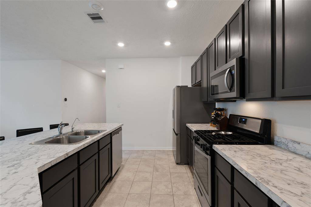 Modern kitchen with dark cabinetry, stainless steel appliances, and marble countertops. Features a dual sink and a spacious layout ideal for cooking and entertaining.