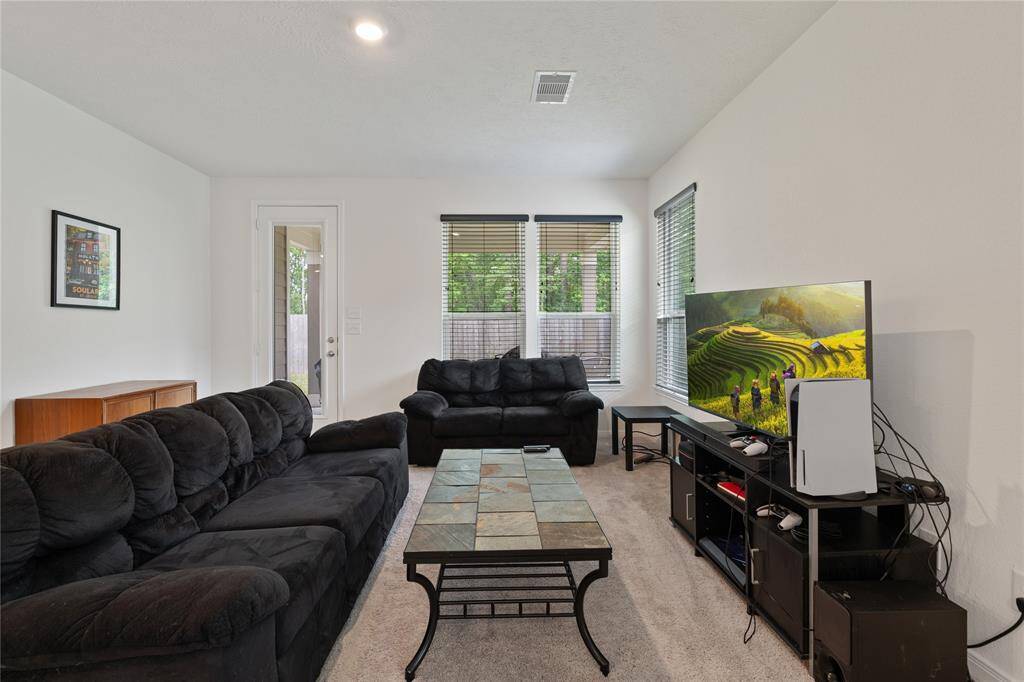 Bright living room with cozy seating, large windows, and a modern entertainment setup. Neutral walls and carpet create a warm, inviting atmosphere. Ideal for relaxation and entertaining.