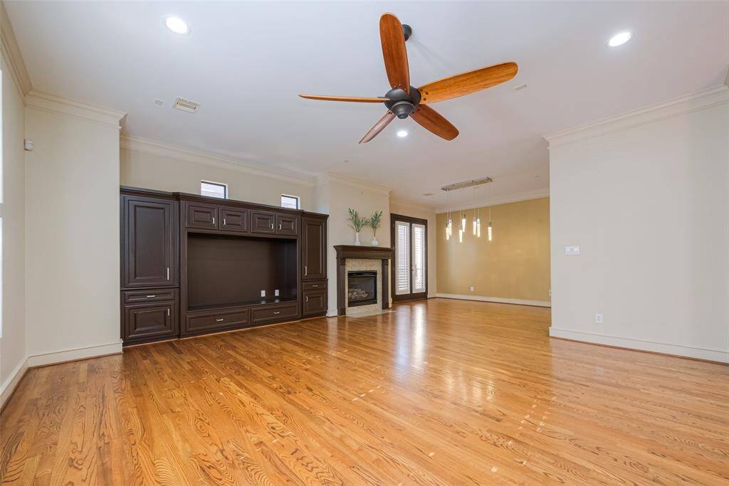 Spacious living room with hardwood floors, a large ceiling fan, and built-in entertainment center. Features a cozy fireplace and ample natural light.