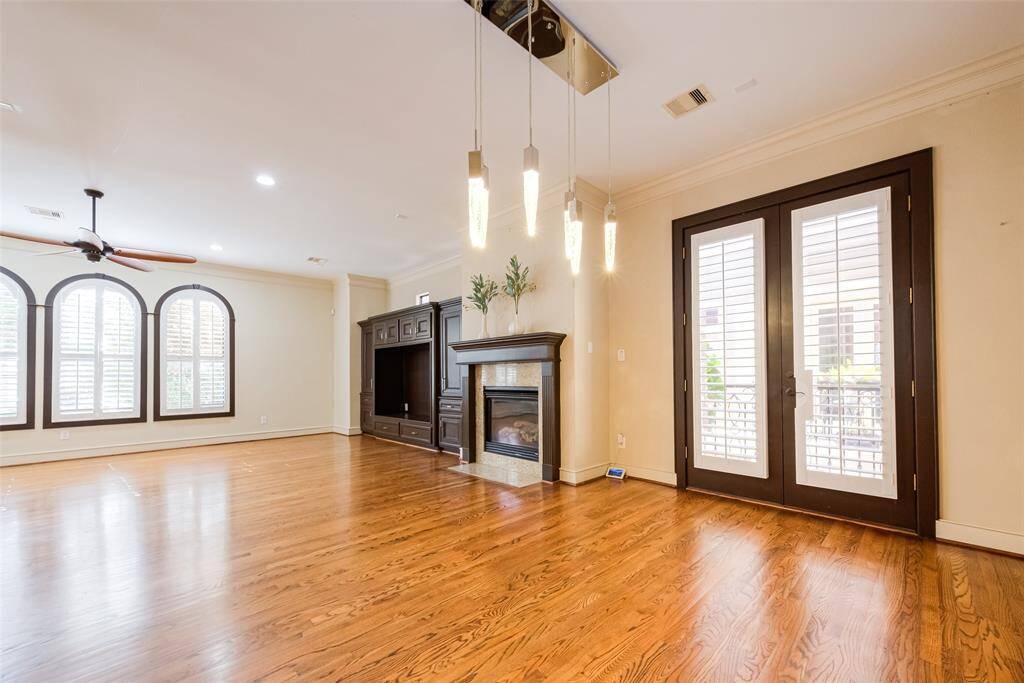 This spacious living area features elegant hardwood floors, a modern fireplace, and built-in shelving. Large arched windows and French doors with shutters offer ample natural light. A stylish ceiling fan and contemporary pendant lights enhance the room's charm.