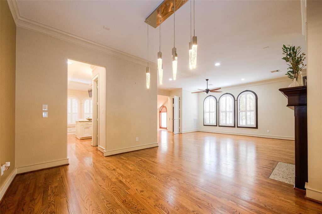 This spacious living area features hardwood floors, recessed lighting, and large arched windows with shutters, offering ample natural light. The open layout includes modern pendant lighting and a ceiling fan, creating a welcoming atmosphere.