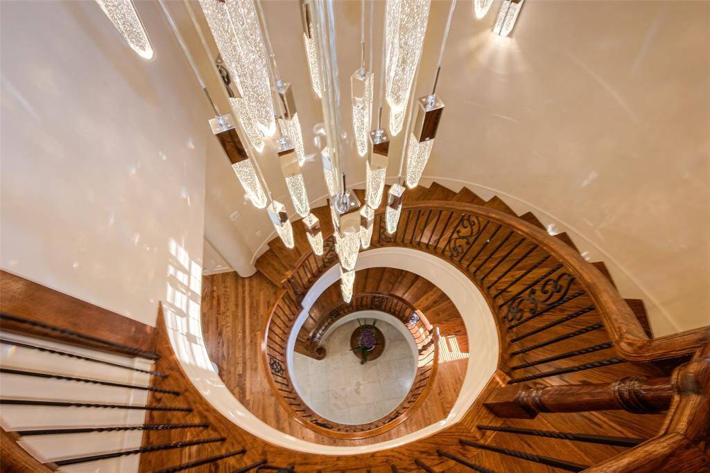This photo showcases a stunning spiral staircase with elegant wooden steps and decorative iron railings, highlighted by a striking modern chandelier. View from the third floor.