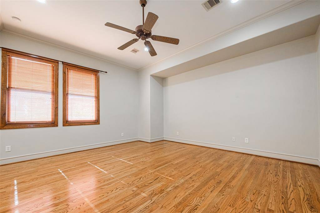 The primary room features hardwood floors, neutral walls, a decorative ceiling fan, and recessed lighting. A doorway leads to an adjacent space, offering potential for a versatile layout.