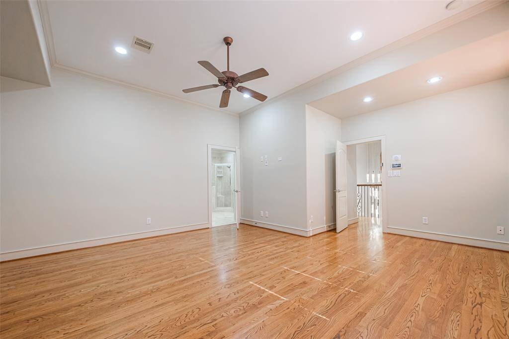 The primary room features hardwood floors, neutral walls, a decorative ceiling fan, and recessed lighting. A doorway leads to an adjacent space, offering potential for a versatile layout.