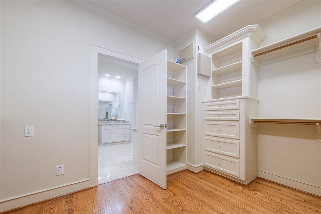 This photo shows a spacious walk-in closet with ample shelving and drawer space, featuring hardwood floors and a doorway leading to the primary bathroom.