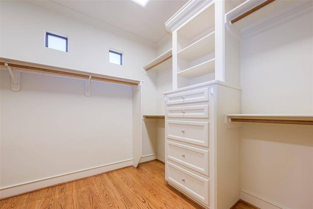 This photo shows a spacious walk-in closet with ample shelving and drawer space, featuring hardwood floors and a doorway leading to the primary bathroom.