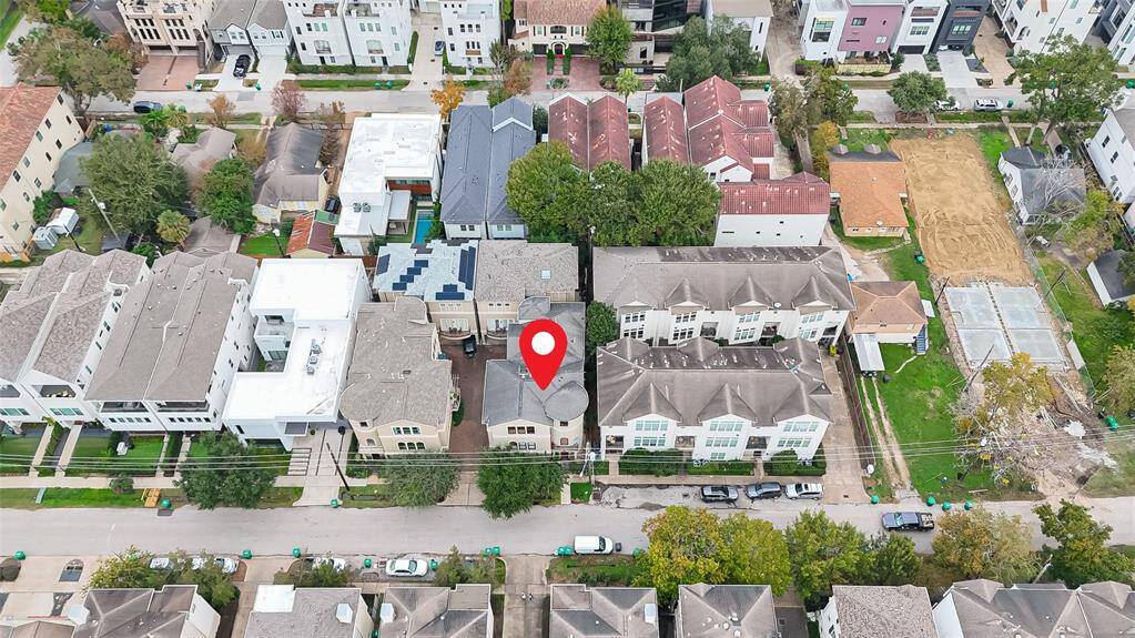 This aerial view of the home showcases a bustling urban neighborhood with a mix of modern and traditional homes. The area is densely populated, featuring tree-lined streets.