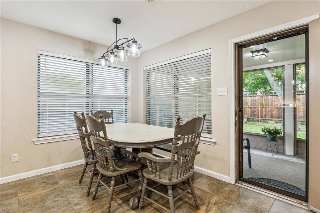 This inviting dining area features large windows with blinds and a stylish overhead light fixture. It opens to a patio with a view of a fenced backyard, providing a perfect blend of indoor and outdoor living.