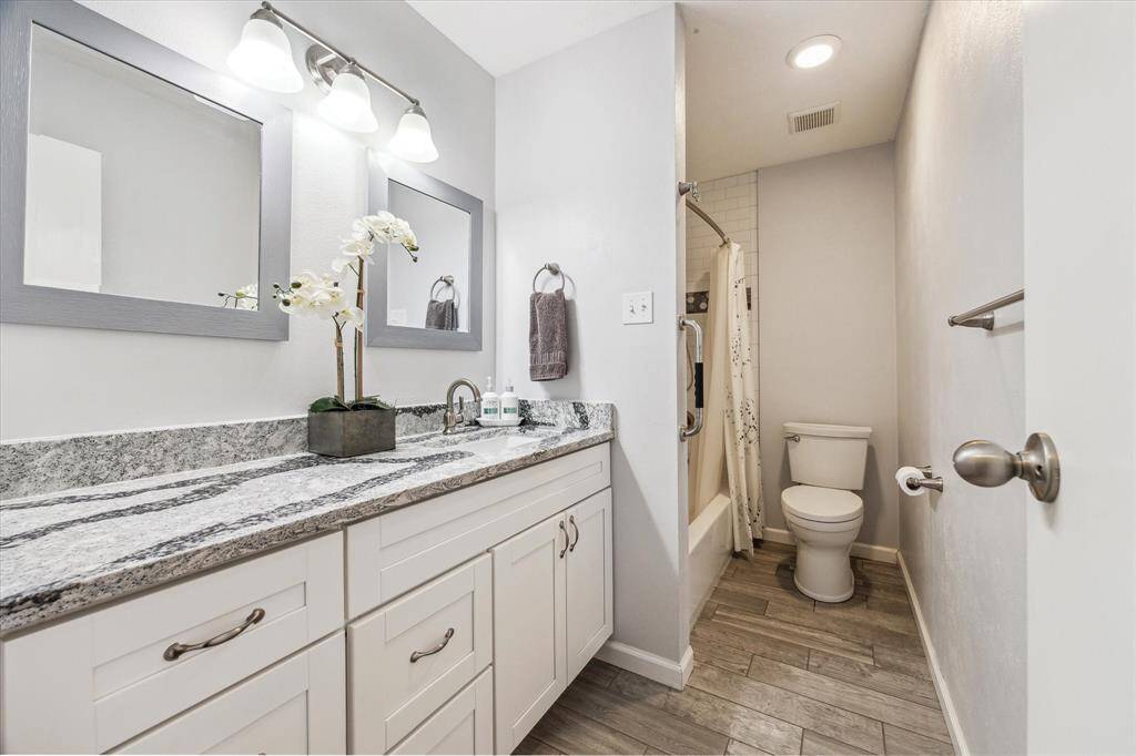 This hallway bathroom features a modern design with a granite countertop, dual mirrors, and a stylish vanity. It includes a shower-tub combo and light tile flooring for a fresh, clean look.