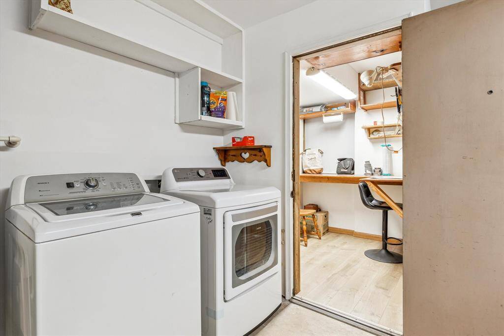 This photo showcases a functional laundry room inside the garage. Adjacent is the small workspace or utility room, featuring a desk, chair, and shelves, ideal for a hobby or storage area.