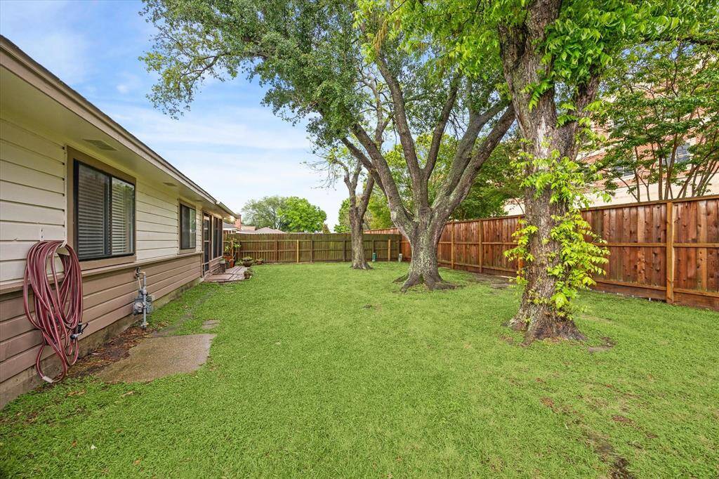 Spacious backyard with lush green grass, two pecan trees, and a well-maintained wooden fence.