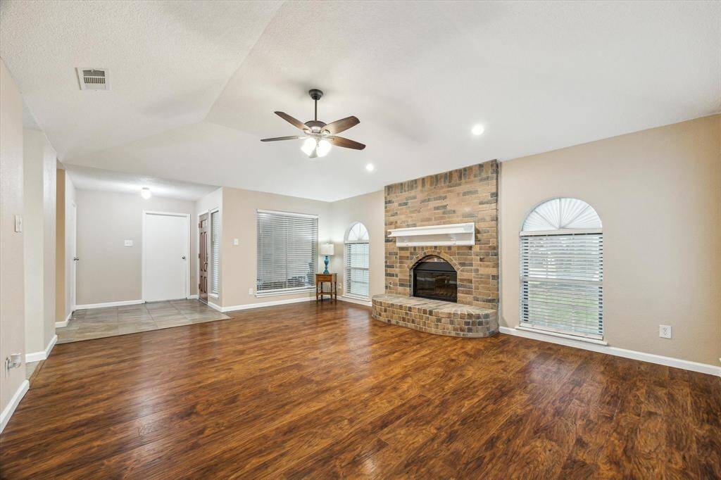 This spacious living room features warm wood flooring, a cozy brick fireplace, and ample natural light.