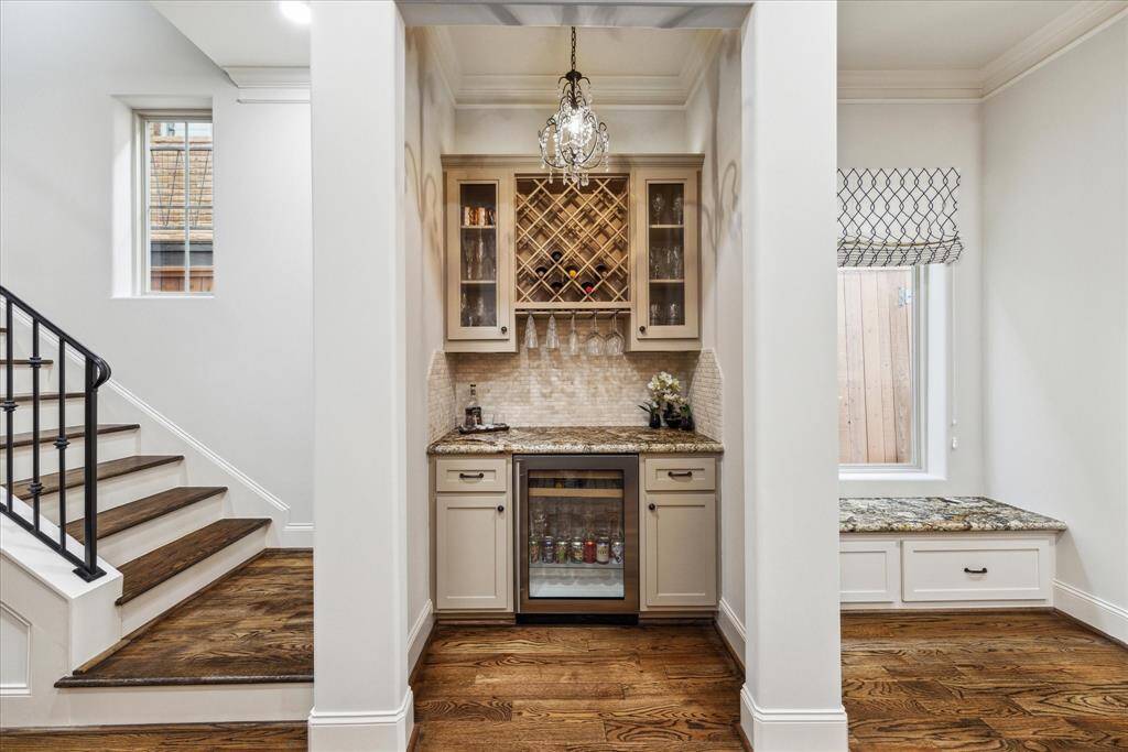 First-floor dry bar featuring built-in wine storage, cabinetry, a wine and beverage cooler, and a sleek granite countertop.