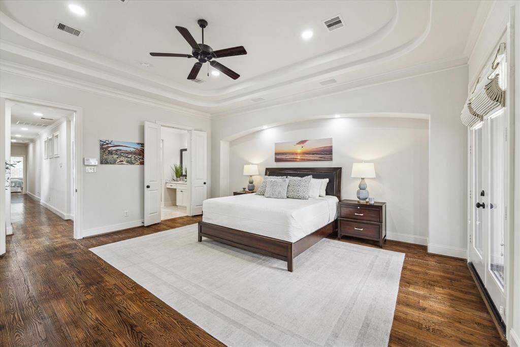 Another view of the primary suite, showcasing a recessed tray ceiling and reading lights above the bed for added ambiance.