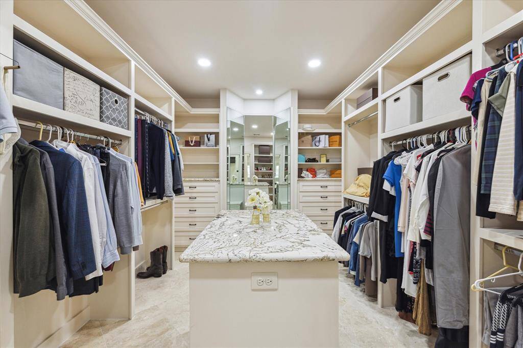 Spacious walk-in closet with built-in shelves and drawers, stainless steel rods, and an island featuring a granite countertop with additional drawers.