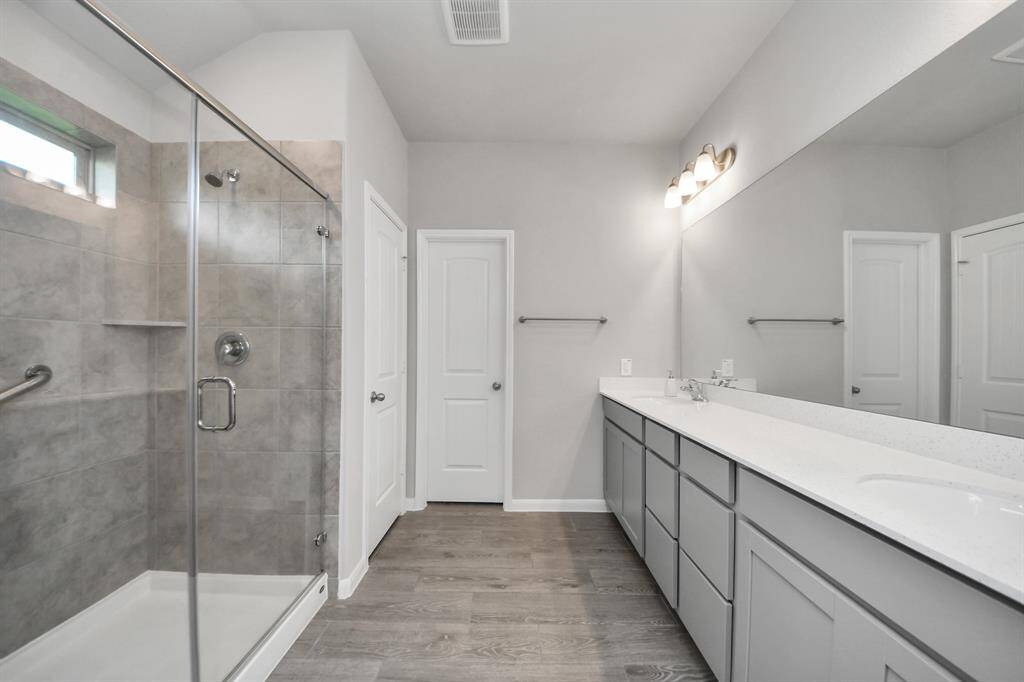 The primary bathroom features dual sinks and a spacious walk-in shower with tile surround and glass door.