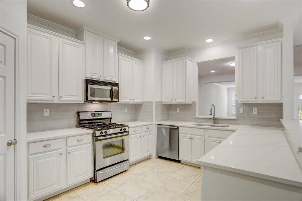 Here’s a closer look at the kitchen layout. It features plenty of cabinet space for storage, stainless steel appliances, and quartz countertops. The door to the left is a large walk-in pantry. The pass-through opens to the living area for added convenience.