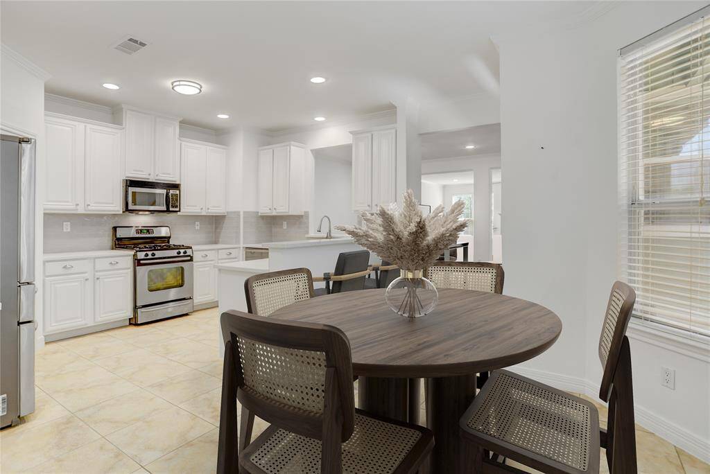 From the cozy breakfast nook, enjoy a clear view into the kitchen, showcasing its crisp white cabinetry, stainless steel appliances, and ample counter space. Just beyond, the open layout continues into the living area, creating a natural flow perfect for entertaining or everyday living. This photo is virtually staged.