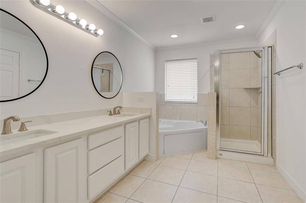 The primary bathroom is spacious and well-appointed, featuring a large dual vanity with updated fixtures and round mirrors. Enjoy a relaxing soak in the oversized tub or a quick rinse in the separate walk-in shower. Neutral tile throughout keeps the space clean and bright, with plenty of room to move around and get ready comfortably.