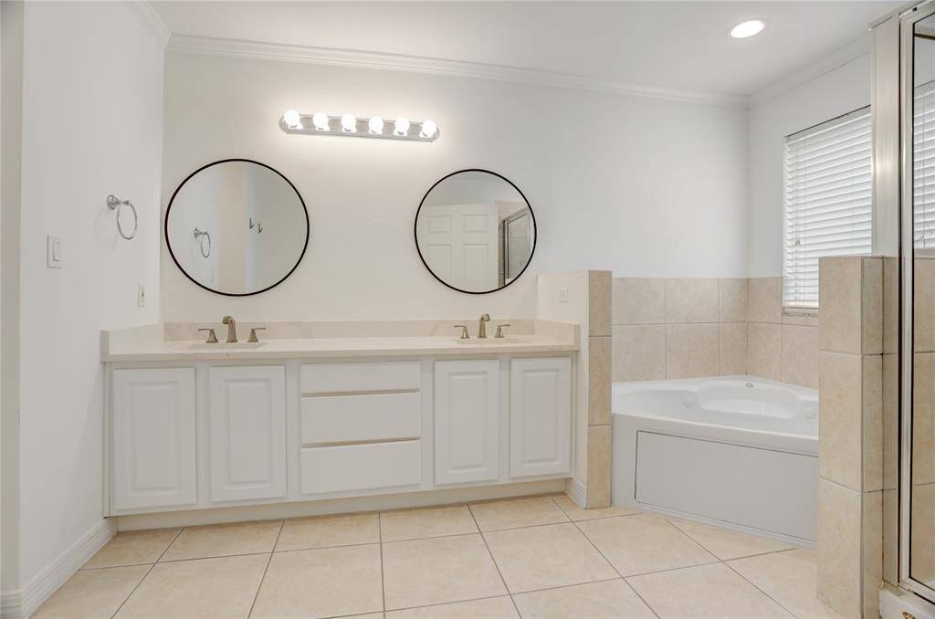 Another view of the primary bathroom highlights the dual sinks with updated fixtures. The corner soaking tub sits beneath a window for natural light, with a separate tiled shower just steps away. Clean lines and neutral tones keep the space simple and functional.
