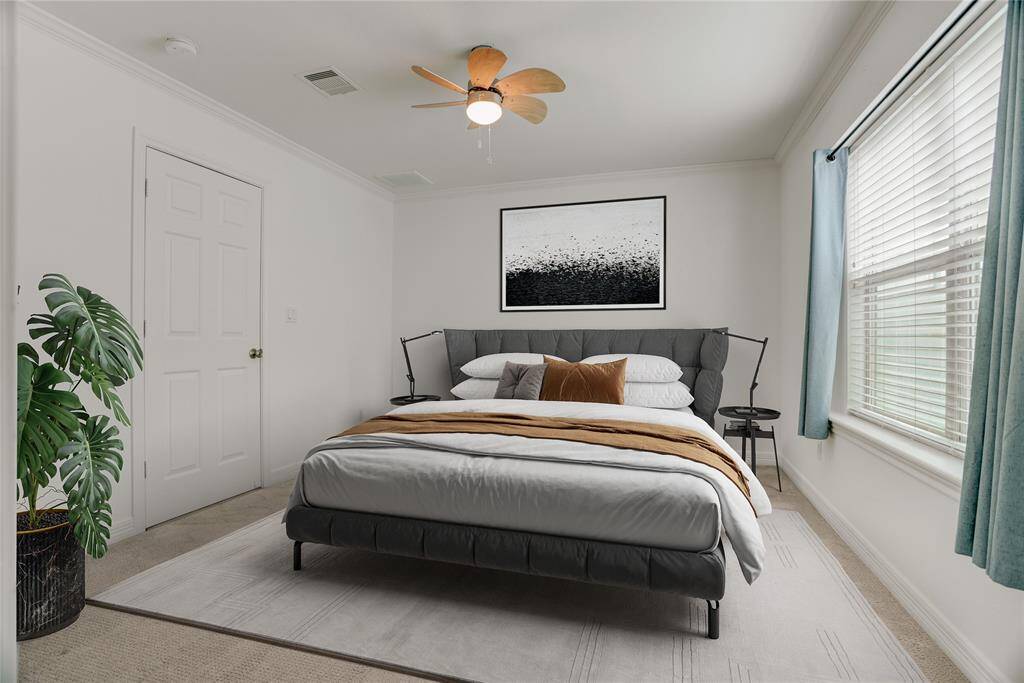 The second bedroom offers a cozy and comfortable space with plush carpeting, crown molding, and a ceiling fan for added comfort. A large window fills the room with natural light. This photo is virtually staged.