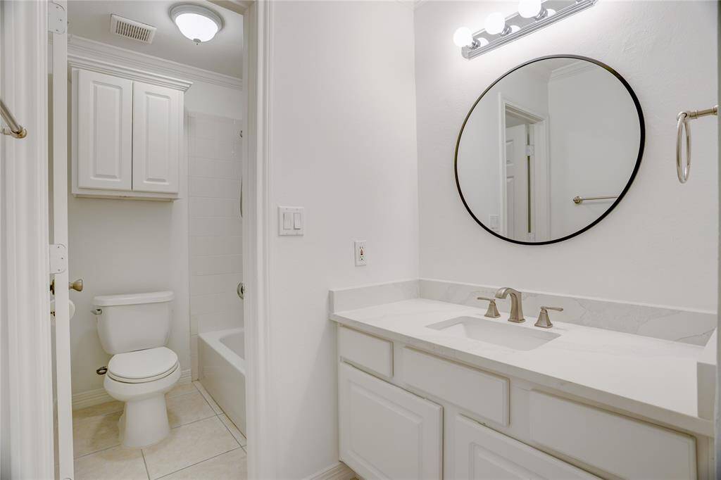 The second full bathroom is located just off the hallway and serves both the second and third bedrooms. It features a quartz countertop vanity with updated fixtures, a round mirror, and a separate area with a tub/shower combo and additional storage above the toilet. Simple and functional for shared use.