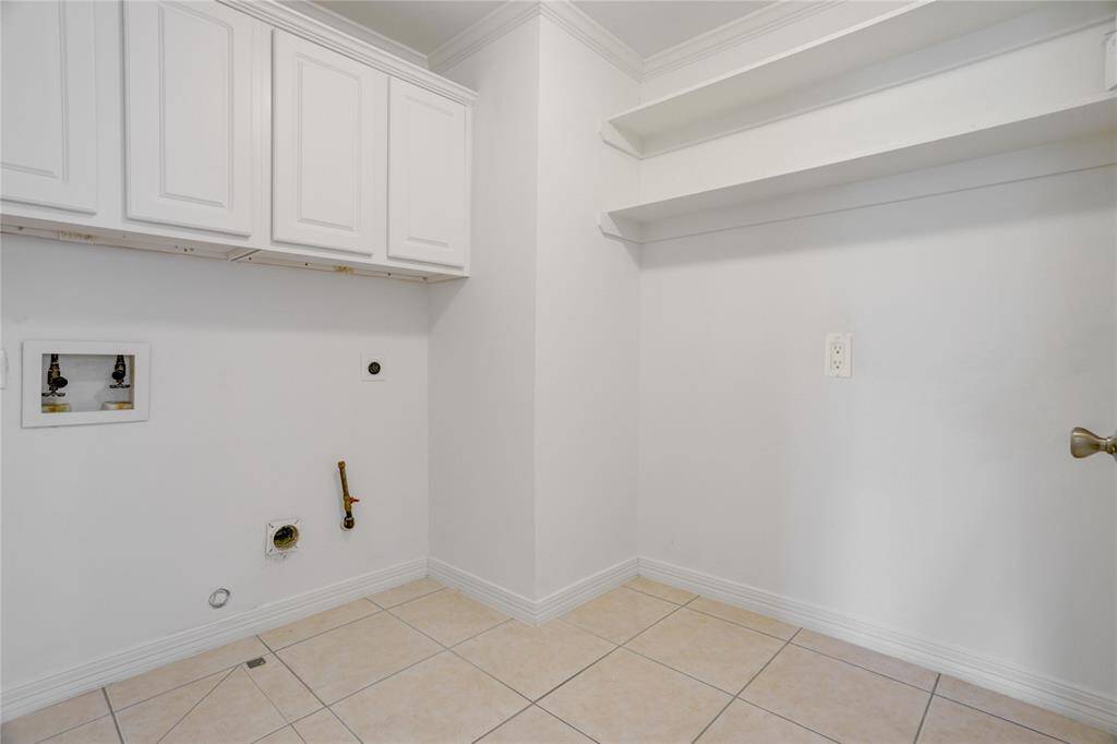 This spacious walk-in laundry room offers plenty of room to work with. It includes upper cabinets for storage, built-in shelving, and tile flooring for easy maintenance. A functional and organized space for handling everyday chores.
