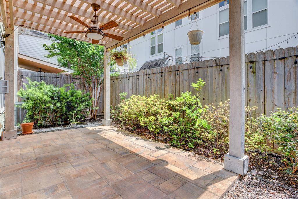 The backyard features a covered patio with a pergola, ceiling fan, and string lights—perfect for relaxing or entertaining. Low-maintenance landscaping and a paved surface make this outdoor space both functional and inviting.