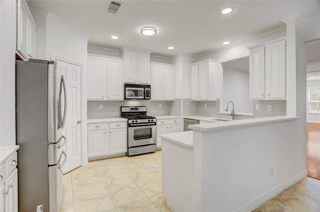 This bright and stylish kitchen is the heart of the home, featuring crisp white cabinetry, sleek quartz countertops, and a neutral tile backsplash that adds a touch of modern elegance. Stainless steel appliances, including a gas range and built-in microwave, provide both function and style. Recessed lighting and a pass-through to the living space enhance the open feel.