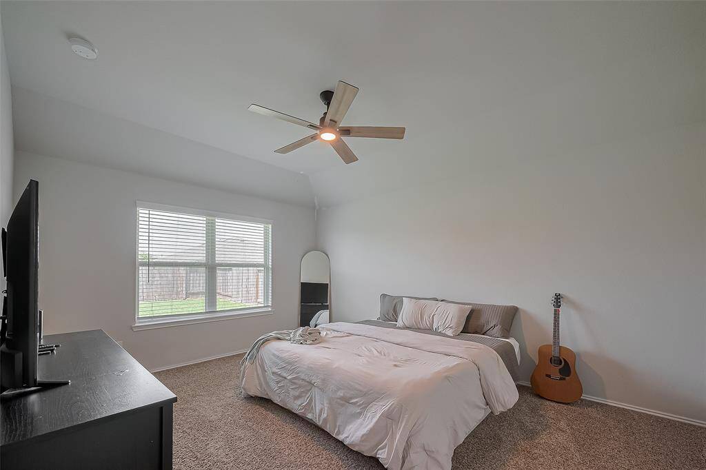 The primary bedroom features a cozy atmosphere with neutral walls and carpet, a ceiling fan, and large window for natural light.