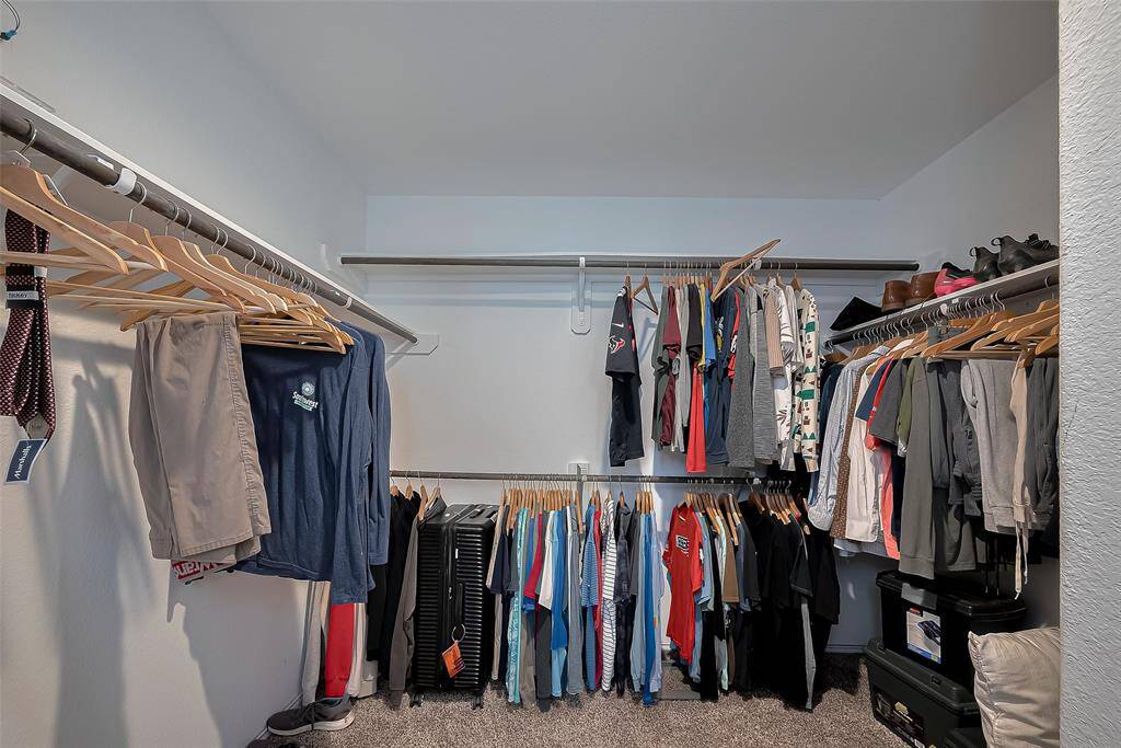 This spacious walk-in closet features ample hanging space with double rods, ideal for organizing clothing. It includes shelving for shoes and accessories, ensuring efficient storage.