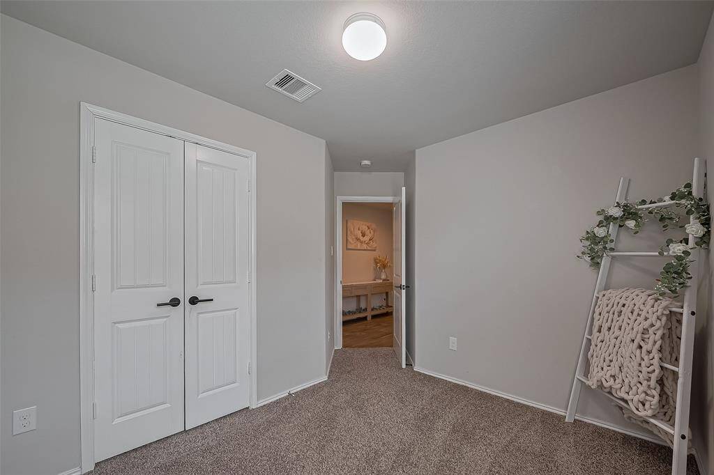 Bedroom 2: A cozy, carpeted room with neutral walls features a double-door closet and simple ceiling light. A decorative ladder with plants and a blanket adds charm. The room leads to a hallway with a glimpse of additional decor.