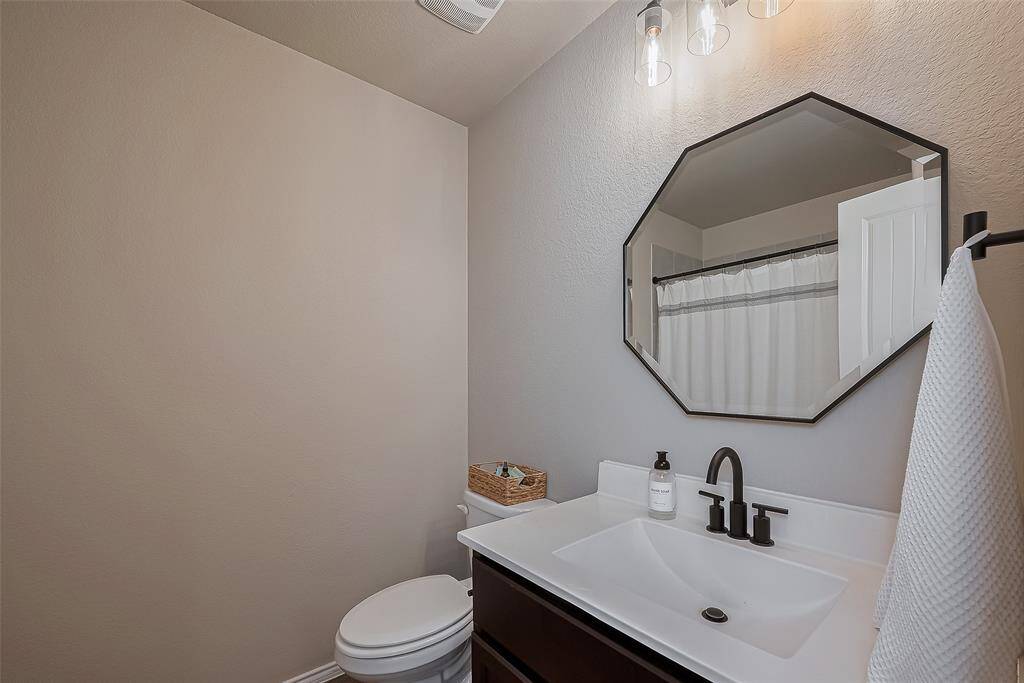 Secondary Bath: featuring a sleek white vanity with a black faucet, an octagonal mirror, and a neutral color palette. The space is well-lit and includes a towel rack and a shower with a curtain.