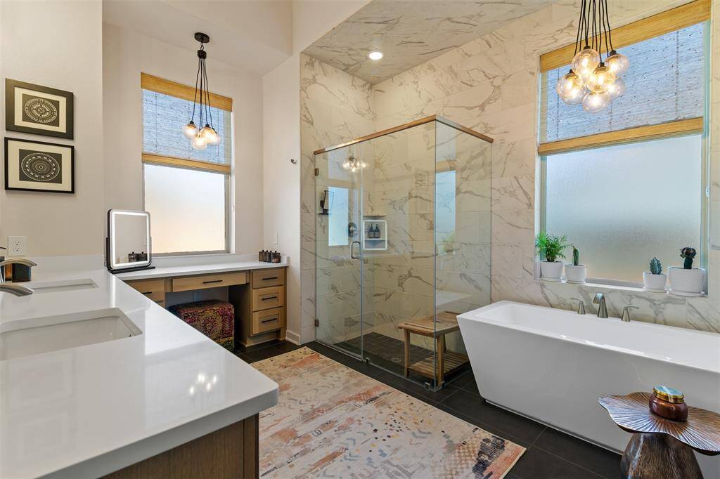 Another view of the primary bathroom showing the soaking tub and chandelier above it along with windows with custom shades.