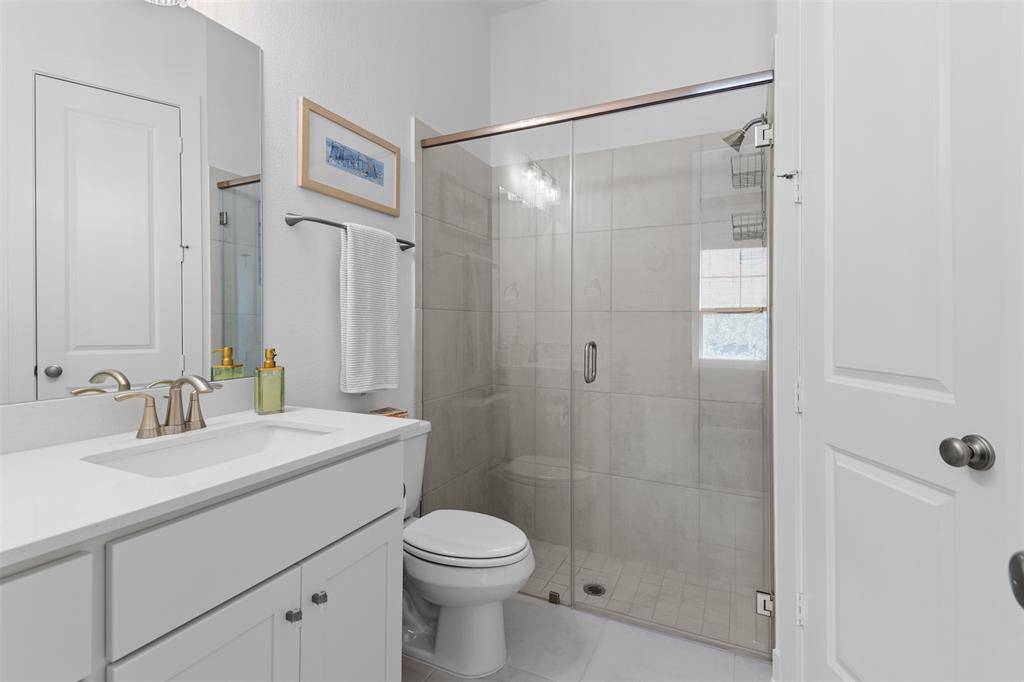 Secondary bedroom's ensuite bathroom with tile floors, large shower with beautiful tile work, frameless shower enclosure, quartz countertop on the vanity and plenty of storage.