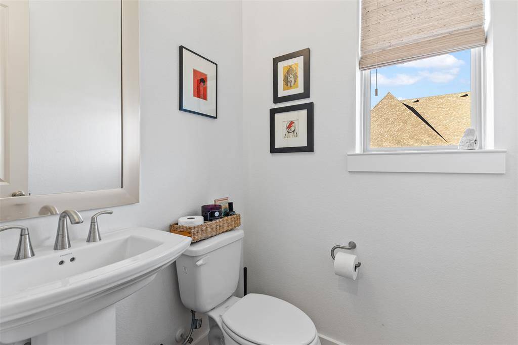 Powder room entryway is from the foyer. Spacious room offers a modern sink, sleek fixtures, and a window with custom shades.