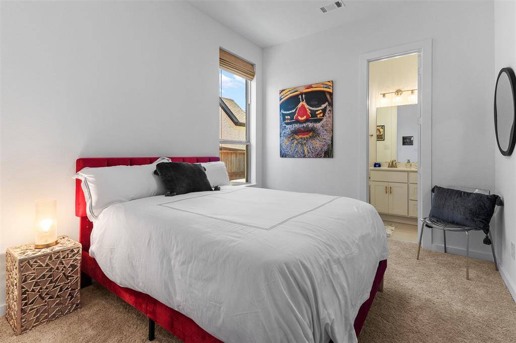 Another secondary bedroom with plush carpet, tall window with custom shade, and an en suite bathroom.