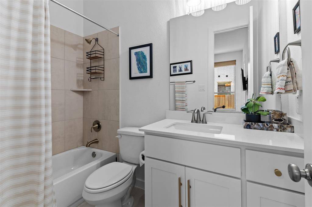 En suite secondary bathroom with shower/tub combo, tile floor, spacious vanity with quartz countertop and lots of storage space.