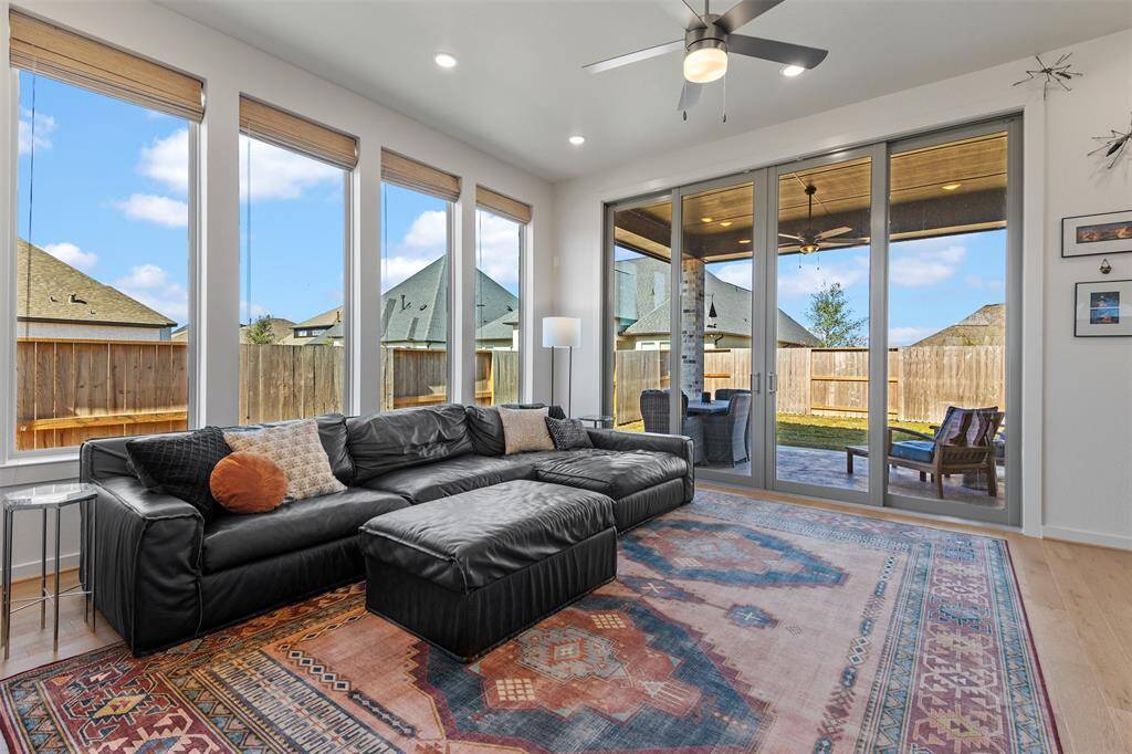 Spacious living room with tall windows, custom shades, engineered wood flooring, fire place, and double sliding glass door to access the patio.