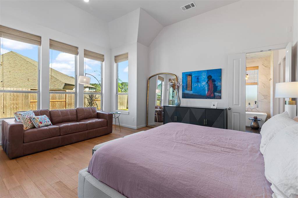 Opposite view of the primary bedroom that shows off the seating area and tall windows with custom shades.