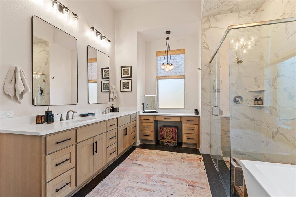 Absolutely stunning large primary bathroom with tile floors, gorgeous custom tile work in the shower and behind the soaking tub, beautiful chandeliers, loads of storage space, double vanities, and a make up area.
